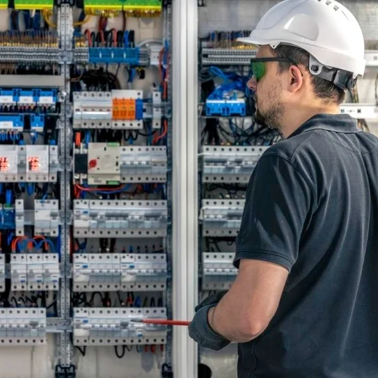 Electrical engineer inspecting a distribution board with protective gear ensuring system safety and performance - About - E-Abel - E-Abel - About - E-Abel - E-Abel Ingénieur électricien inspectant un tableau de distribution avec un équipement de protection garantissant la sécurité et les performances du système
